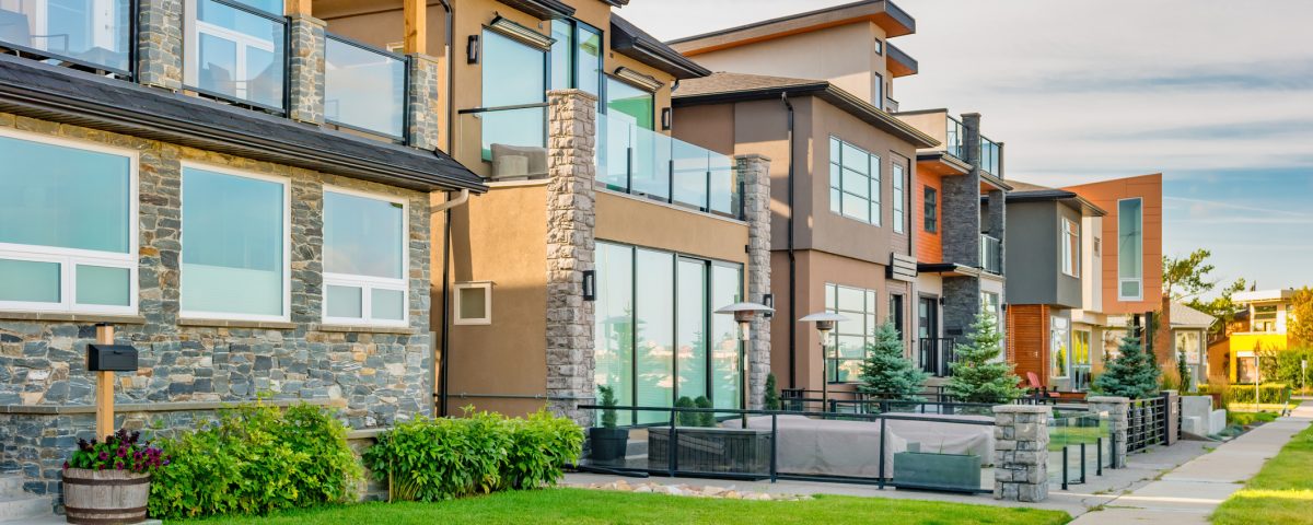 Row of modern townhouses with stone accents, large windows and glass balconies along a green lawn. (informative, concise)