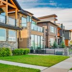 Row of modern townhouses with stone accents, large windows and glass balconies along a green lawn. (informative, concise)
