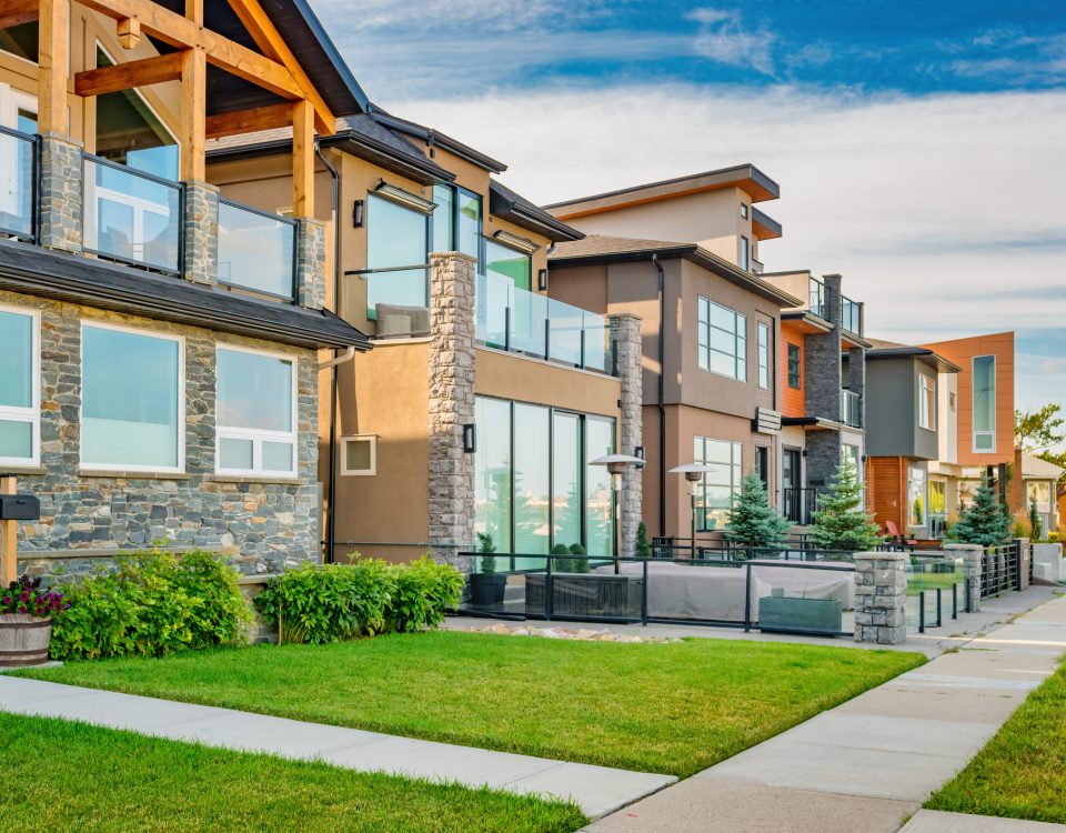 Row of modern townhouses with stone accents, large windows and glass balconies along a green lawn. (informative, concise)